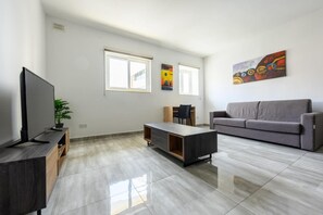 Una sala de estar moderna con un televisor de pantalla plana, un sofá gris, una mesa de centro y una planta.