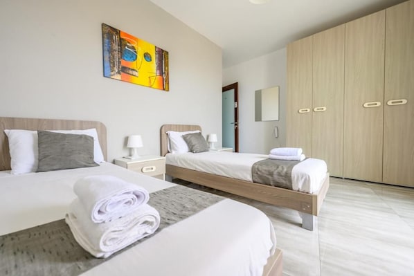 A hotel room with two beds, a large wardrobe, and a painting on the wall. - ATLANTIC COURT F8 (Msida)