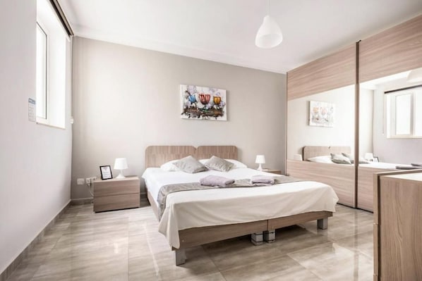 Un dormitorio moderno con una cama grande, mesitas de noche, un tocador, un espejo y obras de arte en la pared.