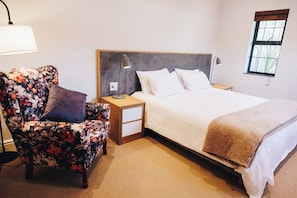 Quarto de hotel com uma cama, mesa de cabeceira, cadeira e janela.