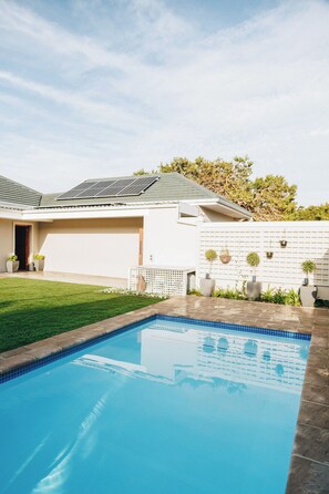 Uma piscina com borda azulejada, um gramado e um edifício com telhado inclinado.