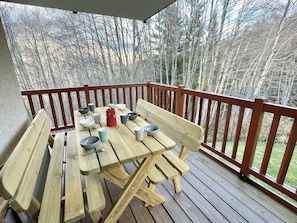 En træterrasse med et picnicbord og bænke, omgivet af gelænder, med udsigt over et skovområde.