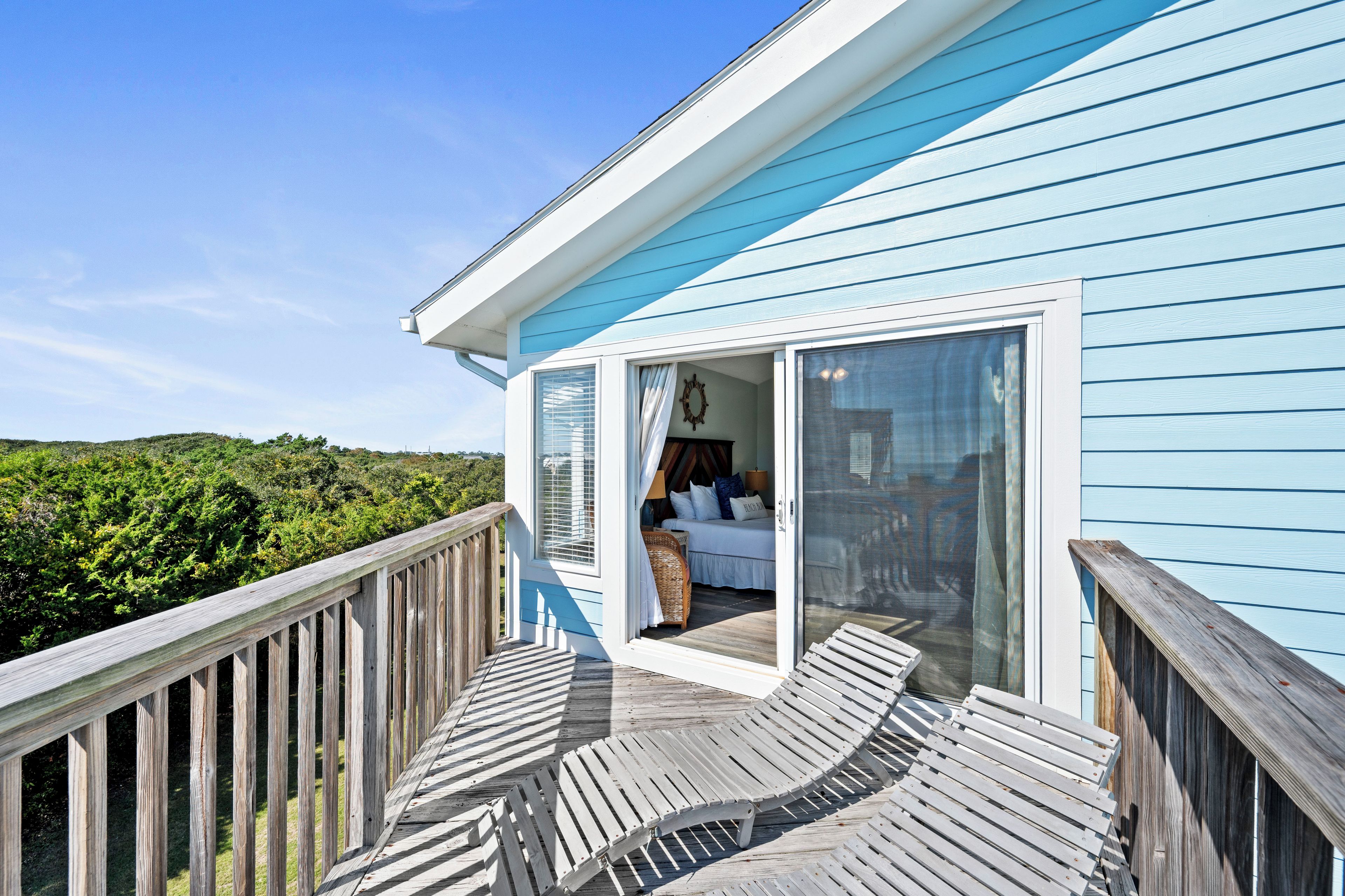A blue building with a wooden deck and a bedroom with a bed and a window.