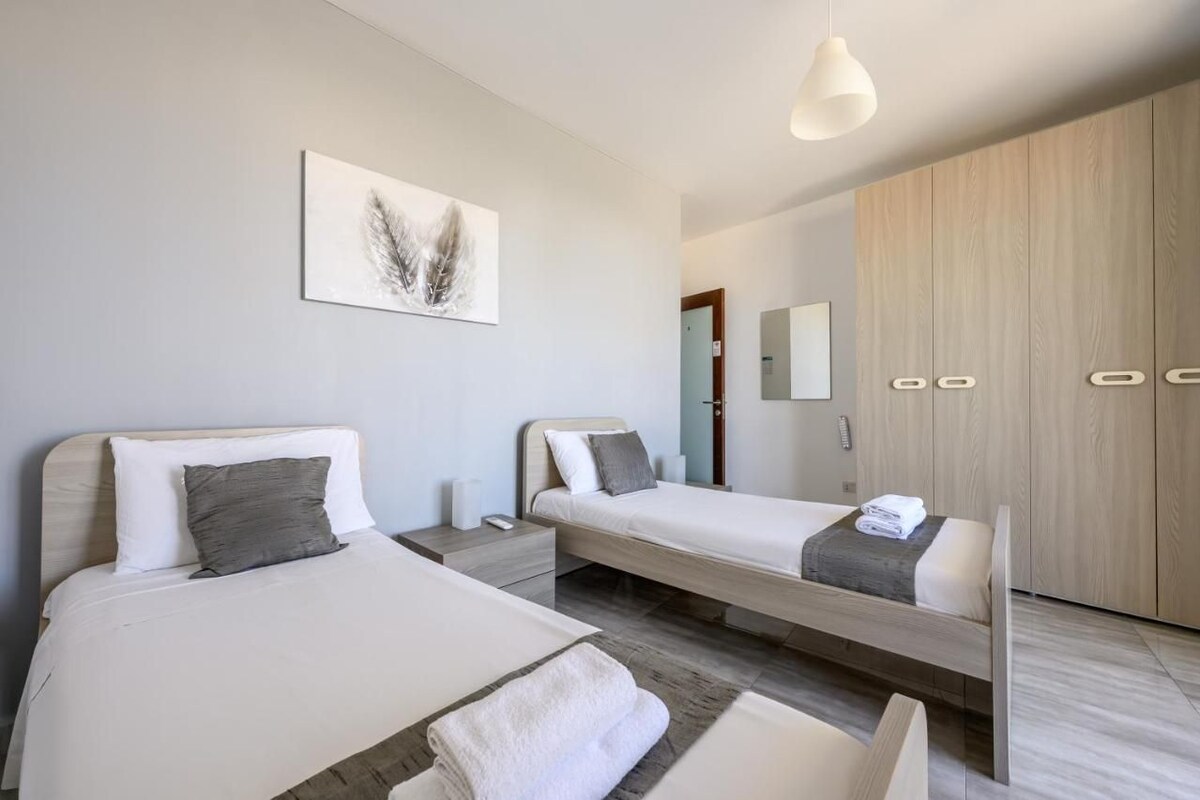 Et moderne hotelværelse med to senge, et stort klædeskab, et natbord med lampe og et billede på væggen.