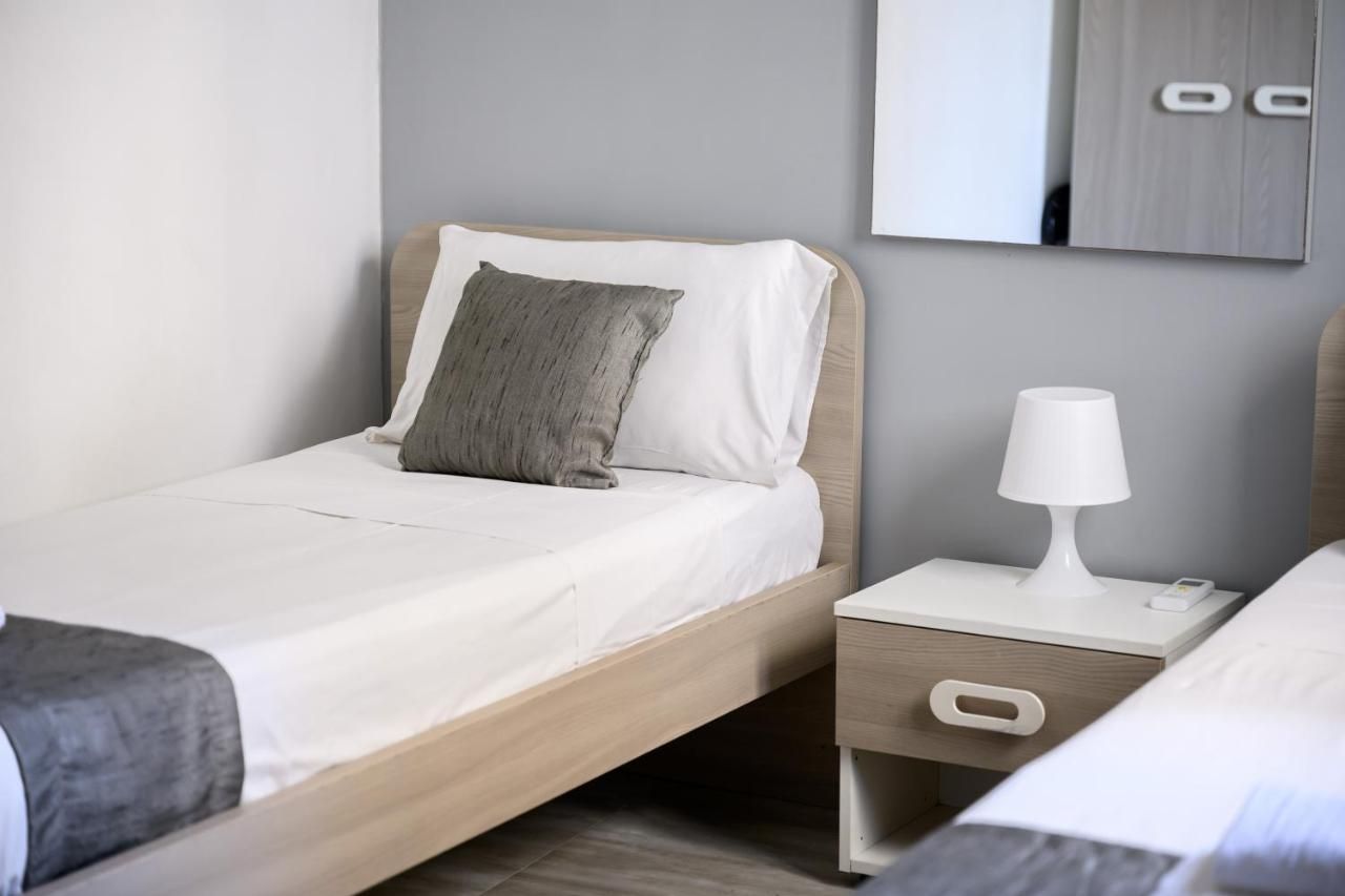 A neatly made bed with a white and gray pillow, a bedside table with a lamp, and a drawer unit.