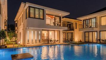 A modern two-story building with a swimming pool, large windows, and outdoor seating areas.