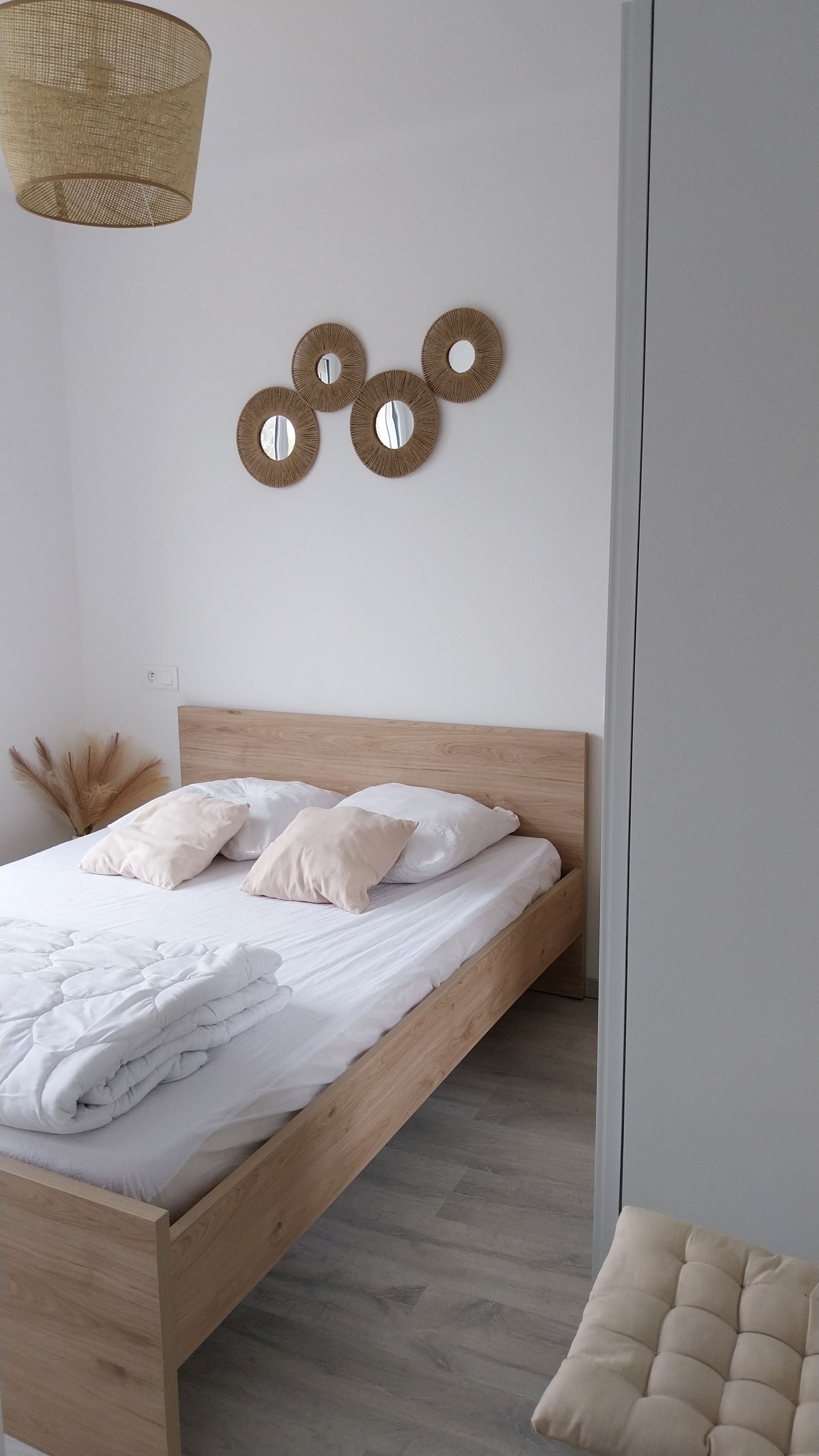 Een bed met houten frame, witte beddengoed en een rond spiegel bevestigd aan de muur.