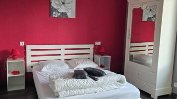 Une chambre avec un lit blanc, des murs rouges, un luminaire suspendu rouge, une table de chevet blanche et une armoire blanche avec un miroir.