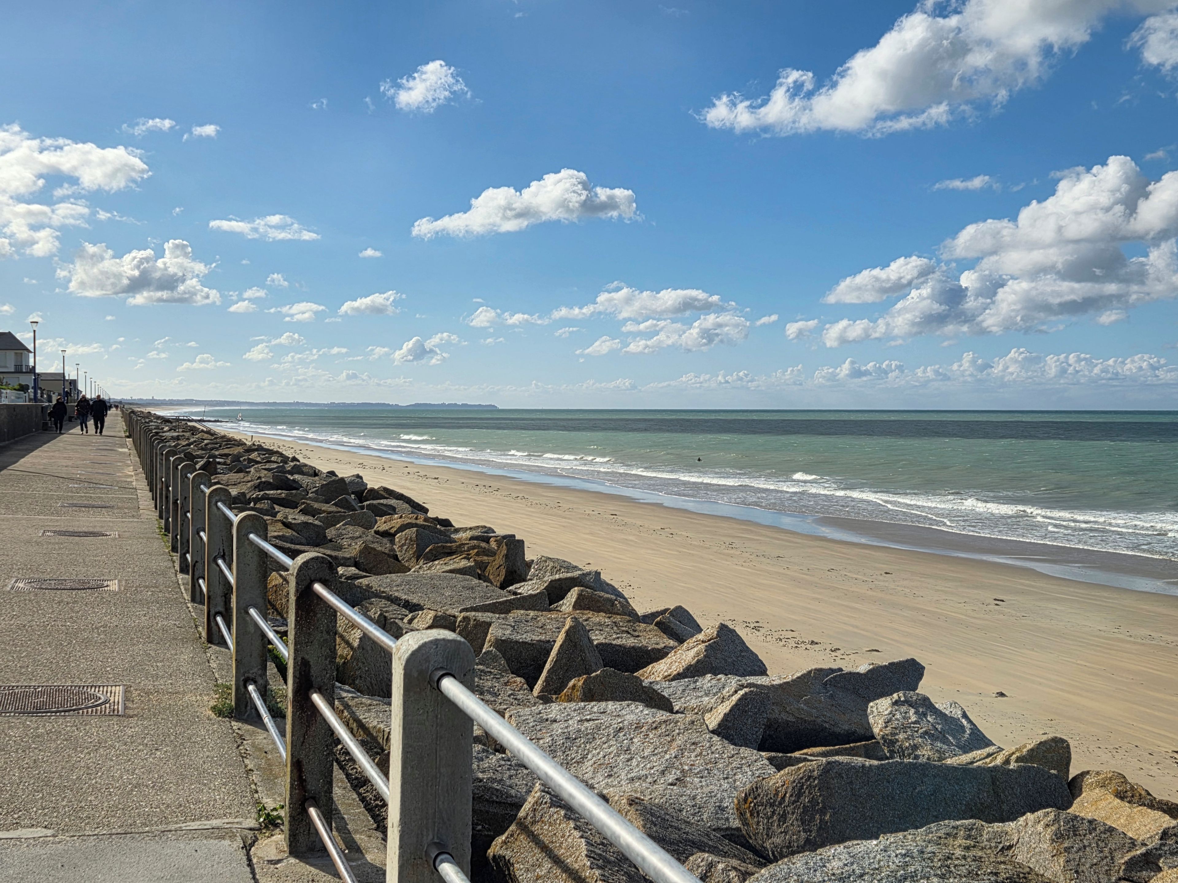 A coastal walkway with a metal railing, leading to a sandy beach.