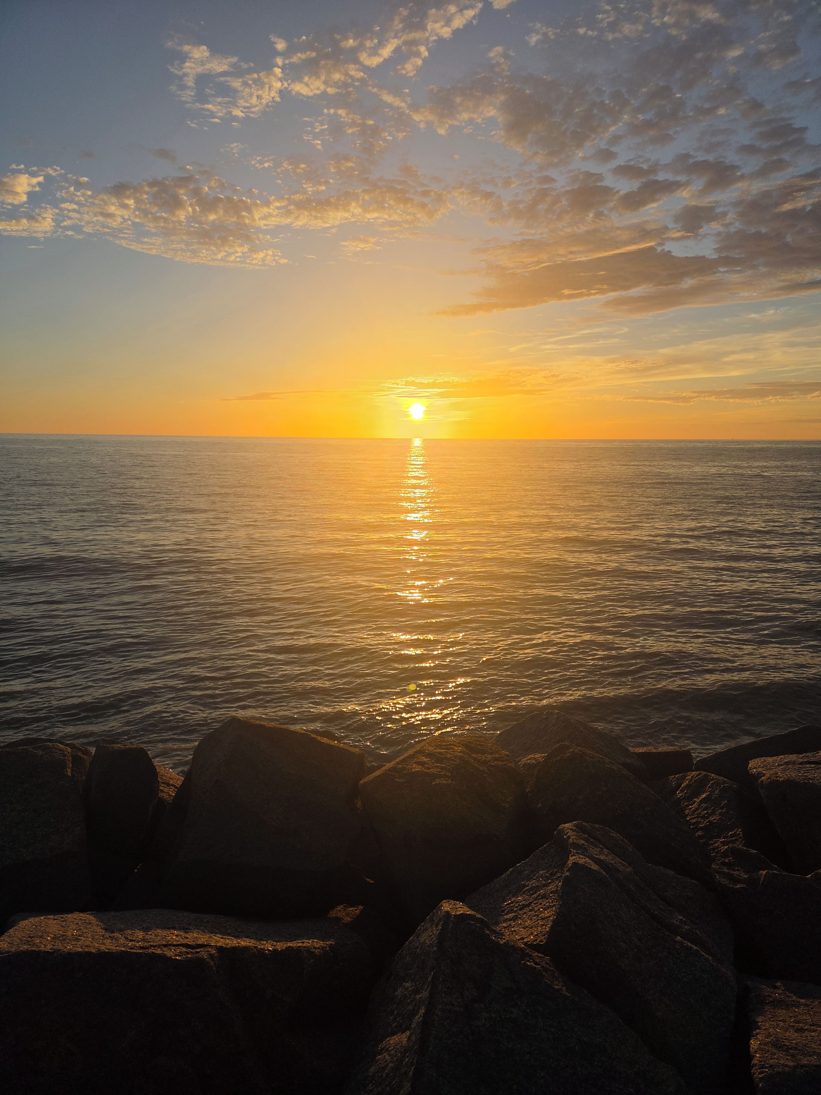 Een zonsondergang boven een rustige zee met rotsen op de voorgrond.