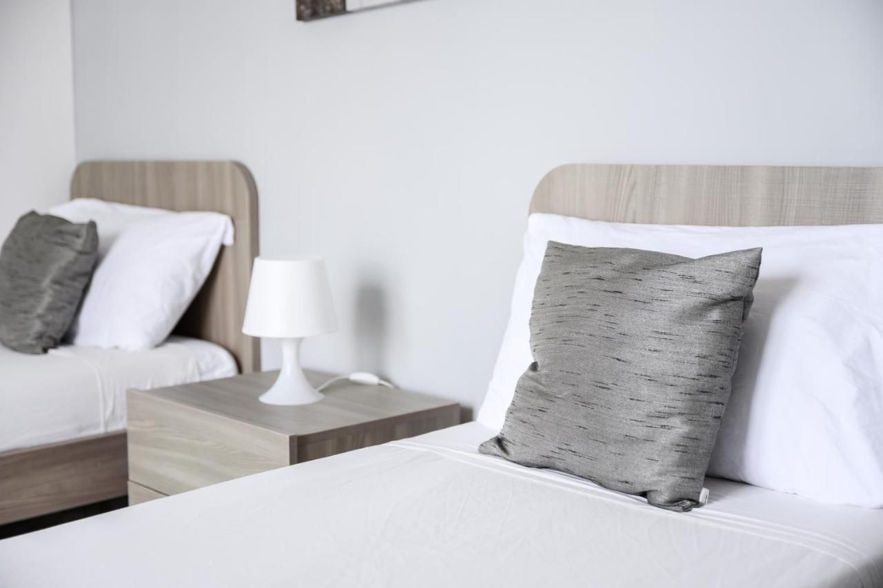 A hotel room with two beds, each with a pillow and a nightstand with a lamp.