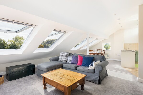 A modern loft apartment with skylights, a grey sectional sofa, a wooden coffee table, and a dining area. - Charming Historic 2 Bed & Parking|Stroud Hill View - Pass the Keys (Stroud)