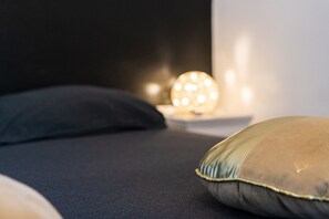 Cama com colchão e travesseiros escuros, mesa de cabeceira com luminária de design arredondado.