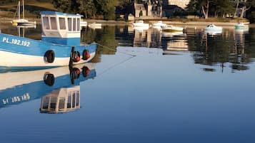 A calm water body with boats docked, a clear sky, and buildings in the background.