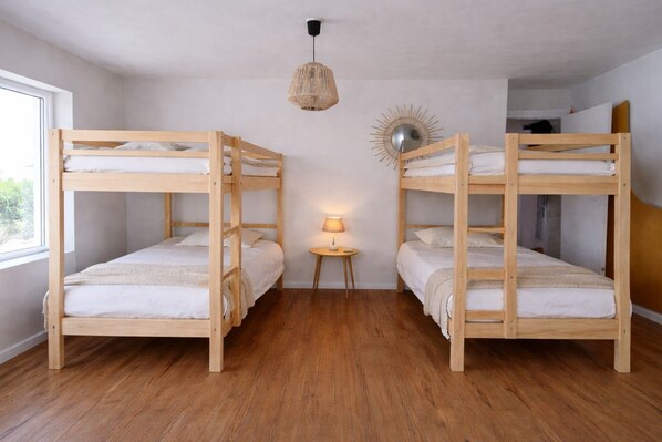 Quarto com duas camas de solteiro, uma mesa redonda pequena com abajur e luminária suspensa.