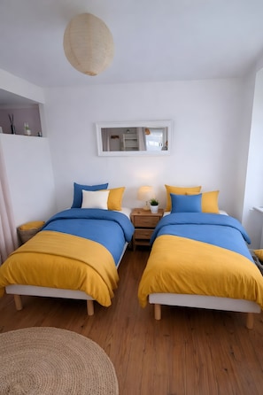 Quarto com duas camas, mesa de cabeceira, abajur e espelho na parede.