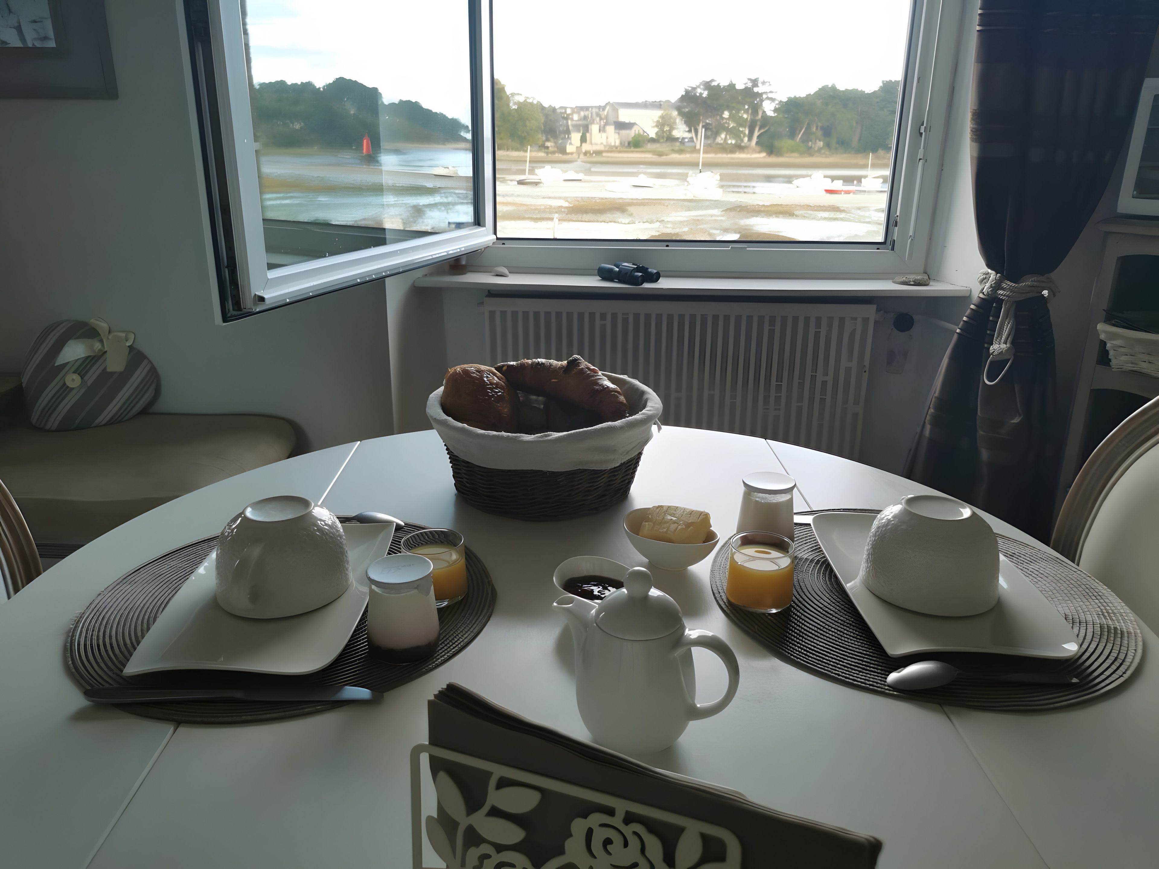 Een ontbijttafel gedekt met een broodmand, waterkoker, kopjes en een melkkruik.