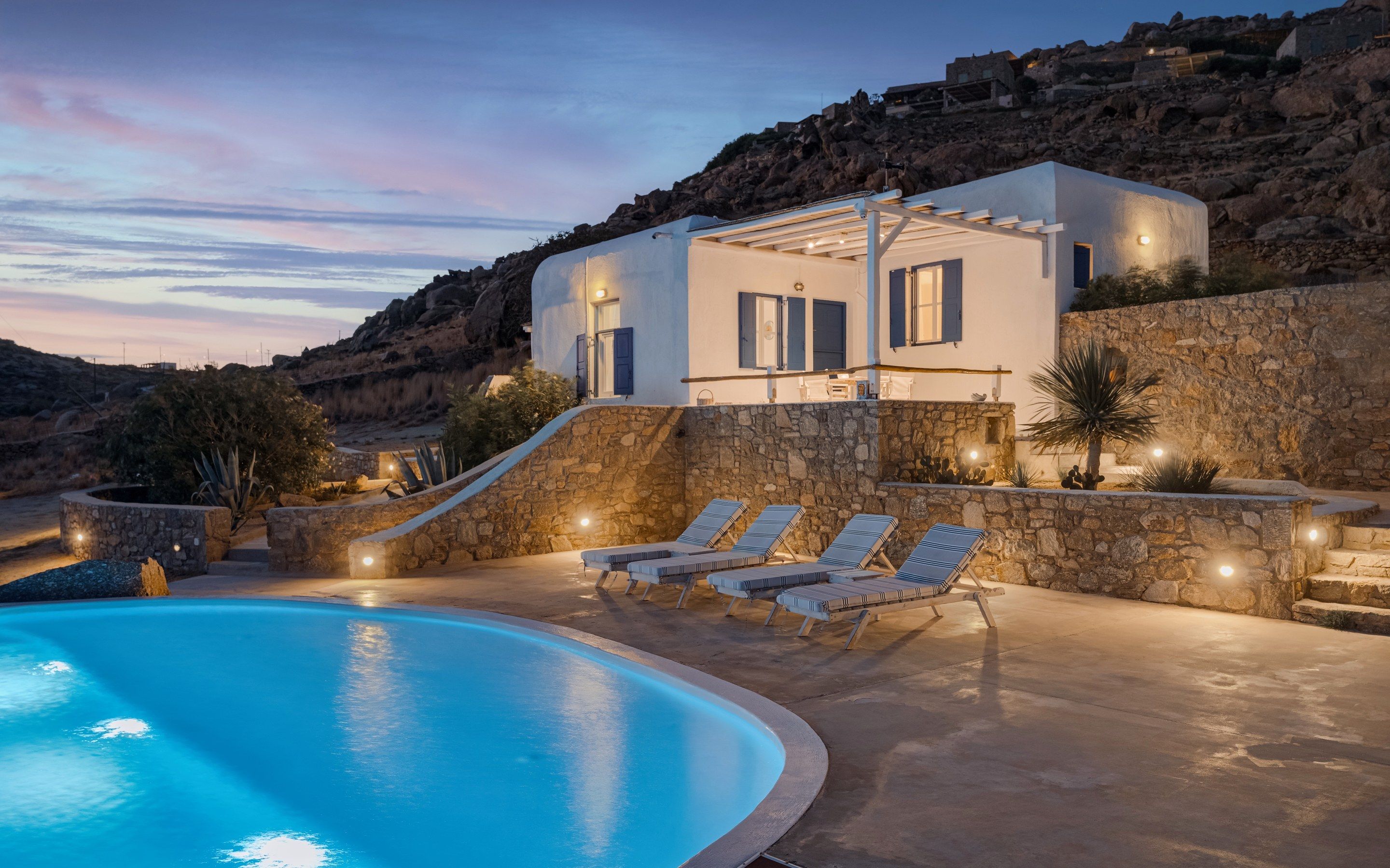 A modern villa with a swimming pool, stone walls, and outdoor seating.