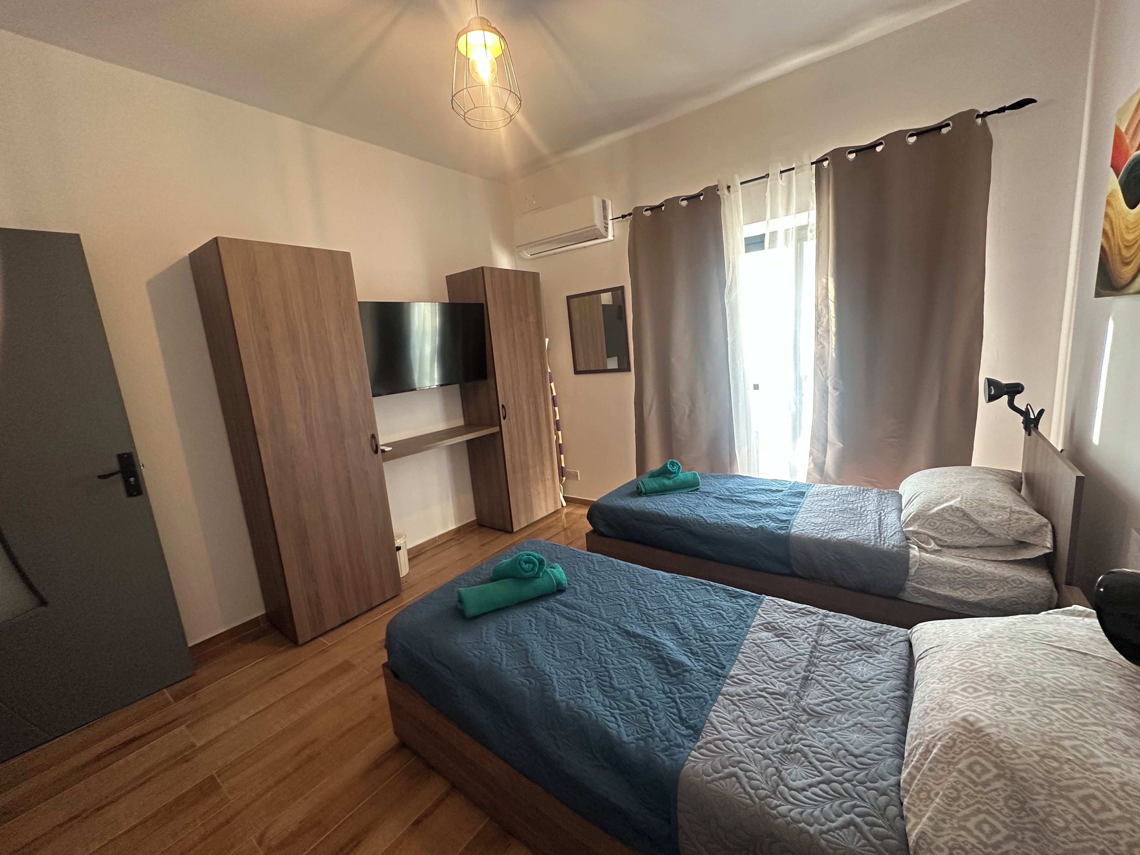 A room with two beds, a TV, a wardrobe, and a window with curtains.