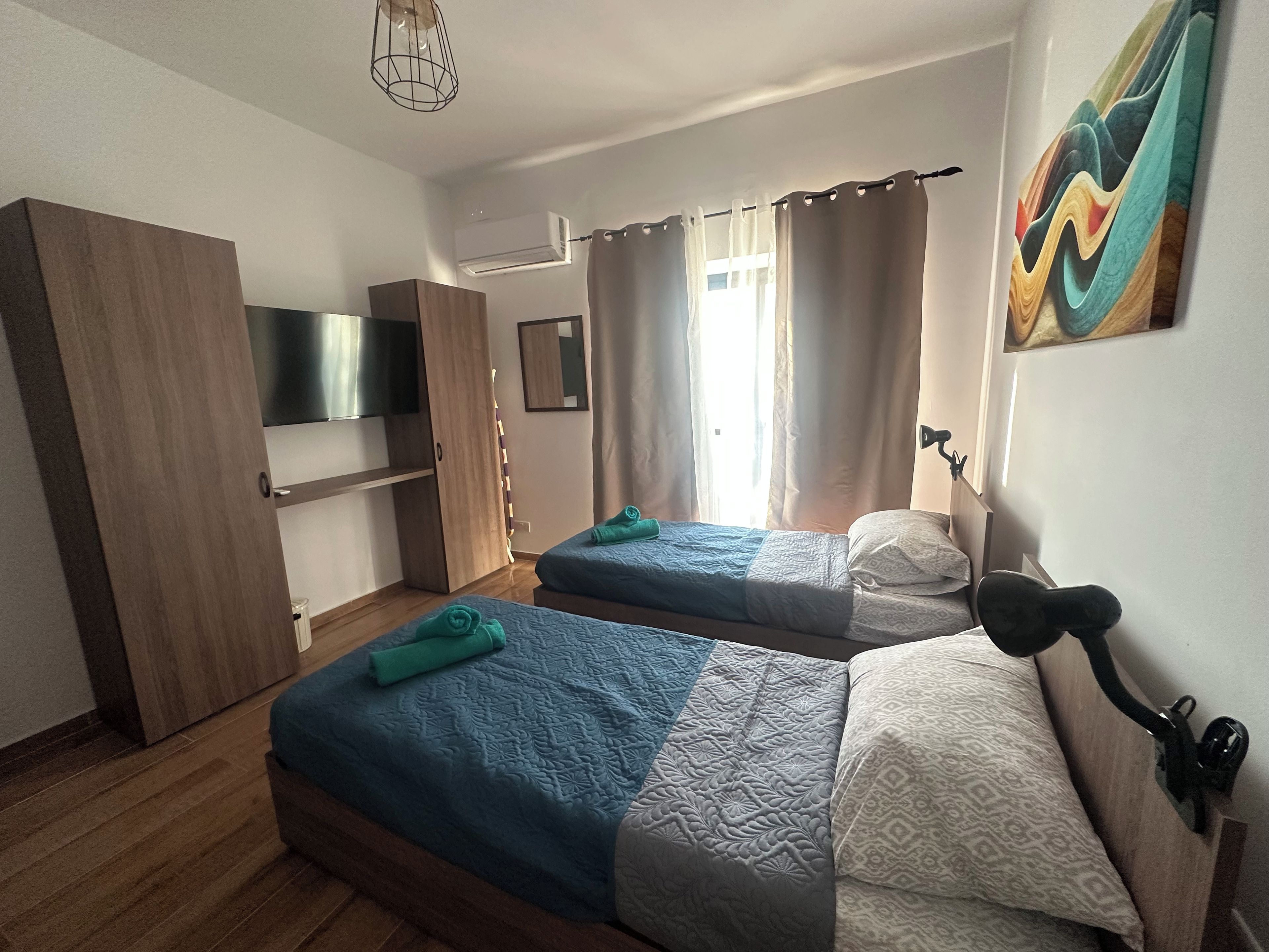 Ein Schlafzimmer mit zwei Betten, einem Fernseher, einem Kleiderschrank und einem Gemälde.