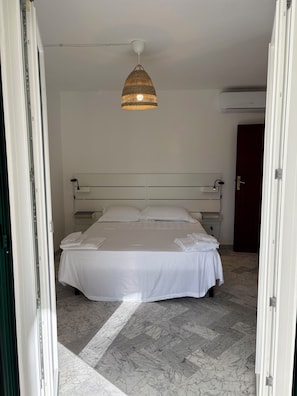 A hotel room with a bed, a hanging light fixture, a door, and an air conditioning unit. - New Listing (Portoferraio)