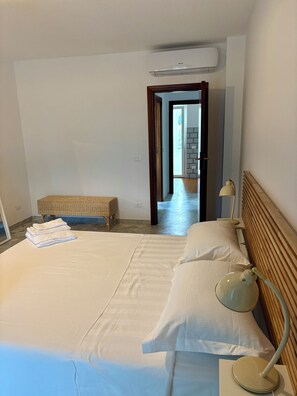 A hotel room with a large bed, a bedside lamp, a bench, and an air conditioning unit. - New Listing (Portoferraio)