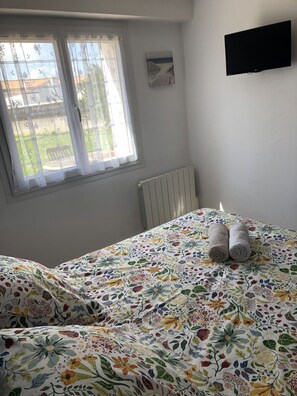 Ein Schlafzimmer mit einem Bett, einem Fenster mit Vorhängen, einem Heizkörper und einem Flachbildfernseher an der Wand.