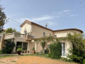 A two-story building with a stone facade, a balcony, and a garden area with potted plants. - New Listing (La Redorte)