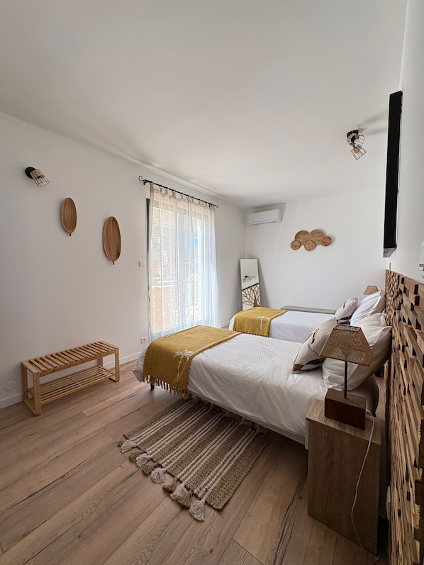 A bedroom with a bed, bedside table, bench, and a window with curtains. - New Listing (La Redorte)