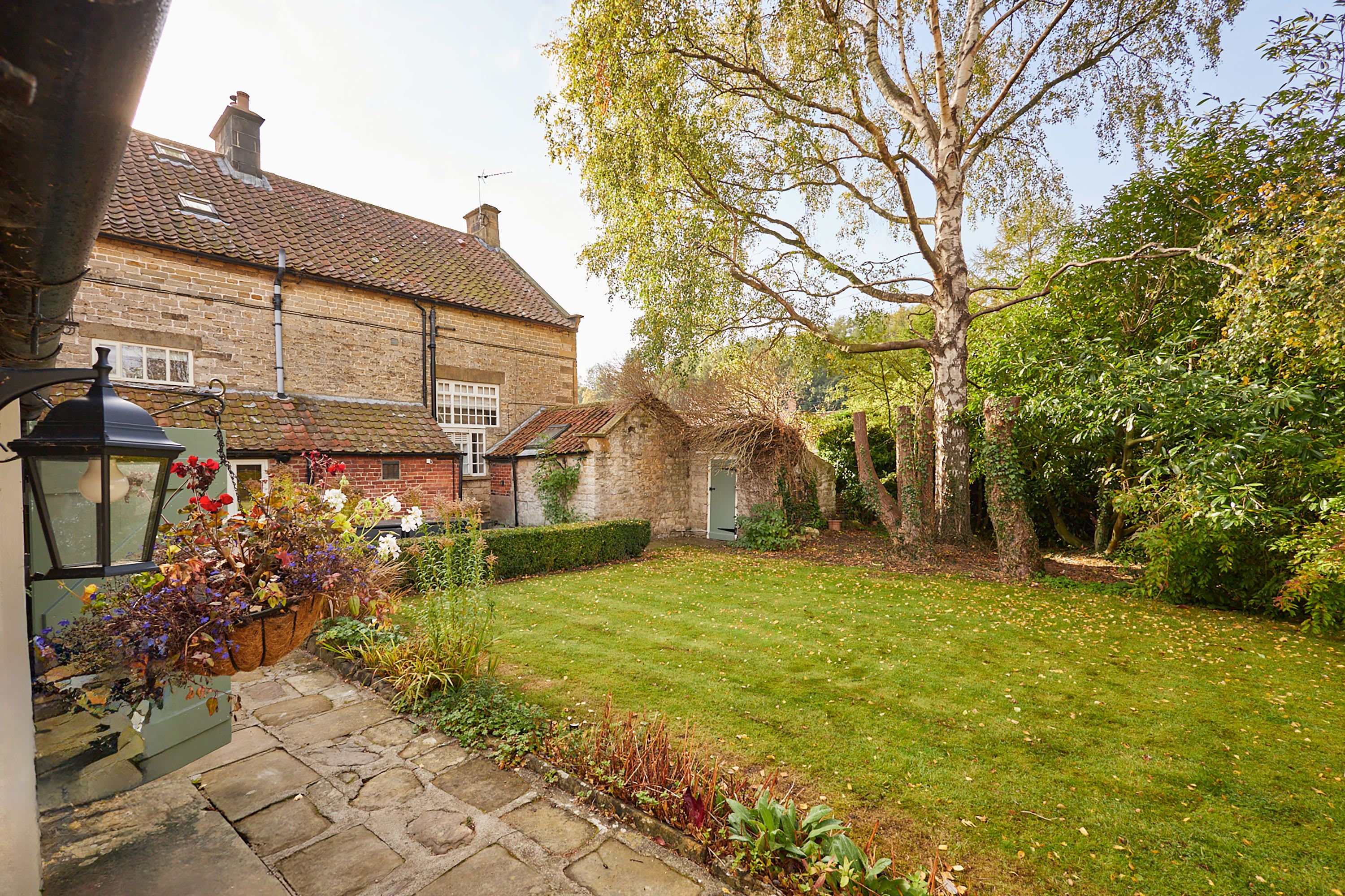 A traditional brick house with a well-maintained garden, stone pathway, and a large tree.