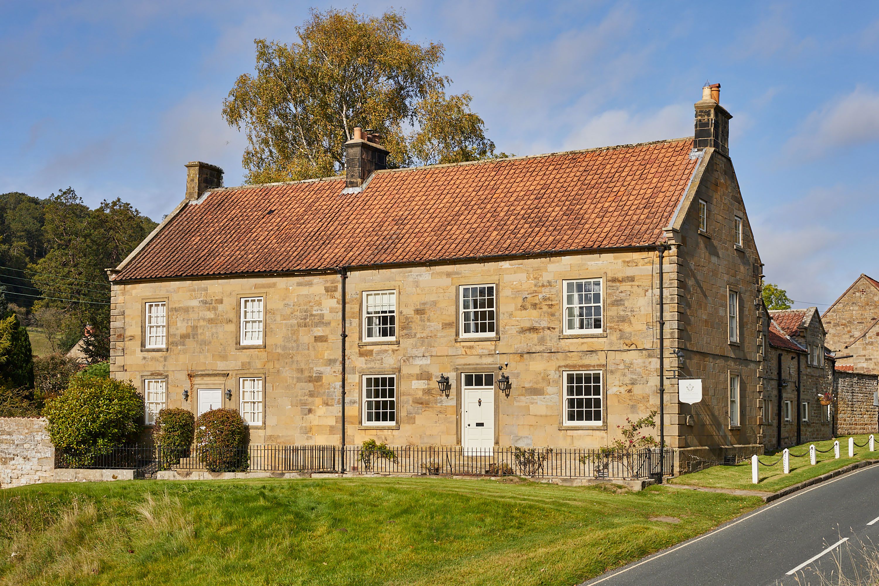 A two-story stone building with a red-tiled roof, multiple windows, and a white door.