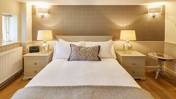 A neatly made bed with white linens, two bedside lamps, a radio, and a small round table with a chessboard.