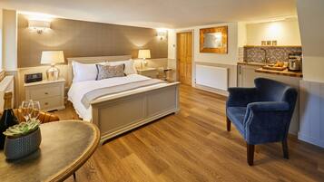 A hotel room with a bed, bedside tables, a chair, a small table with a plant, a mirror, and a kitchenette.