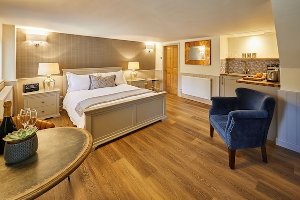 A hotel room with a bed, bedside tables, a chair, a small table with a plant, a mirror, and a kitchenette. - Host & Stay | Ryedale (Hutton-le-Hole)