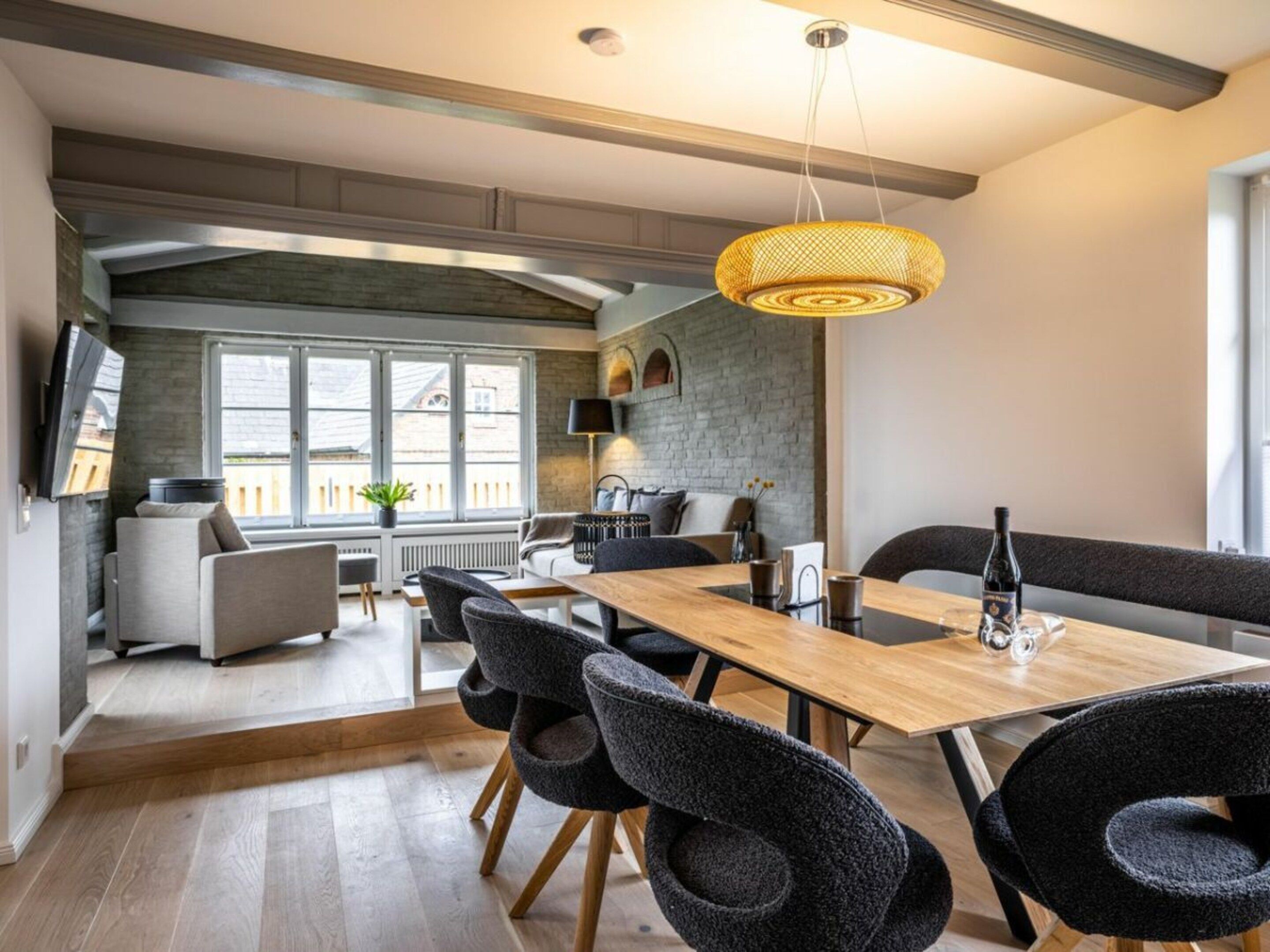 Un espace repas moderne avec une table en bois, des chaises noires et un luminaire suspendu.