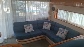A blue sofa with decorative pillows, a window with sheer curtains, and a view of the outside.