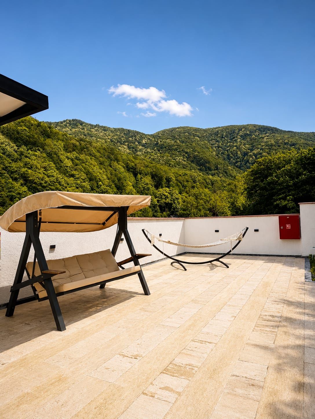 Una terraza en la azotea con una silla colgante y una hamaca, con vistas a un paisaje boscoso.