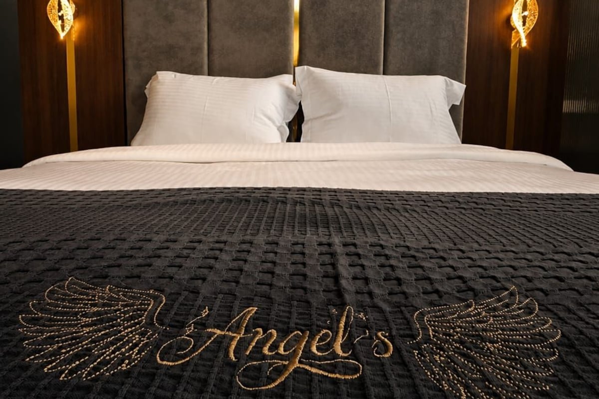 A hotel room with a large bed, a dark textured bedspread, and a headboard with vertical panels.