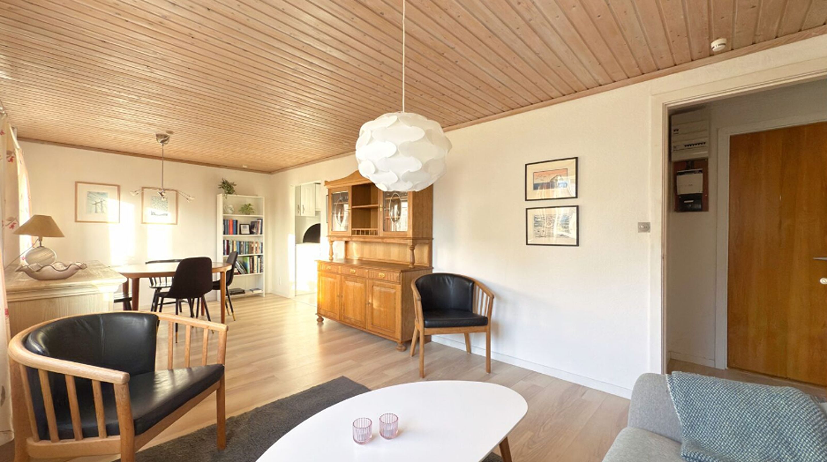 Amplia sala de estar con techo de madera, comedor con mesa y sillas, área de cocina con armarios de madera, y una puerta que da a otra habitación.