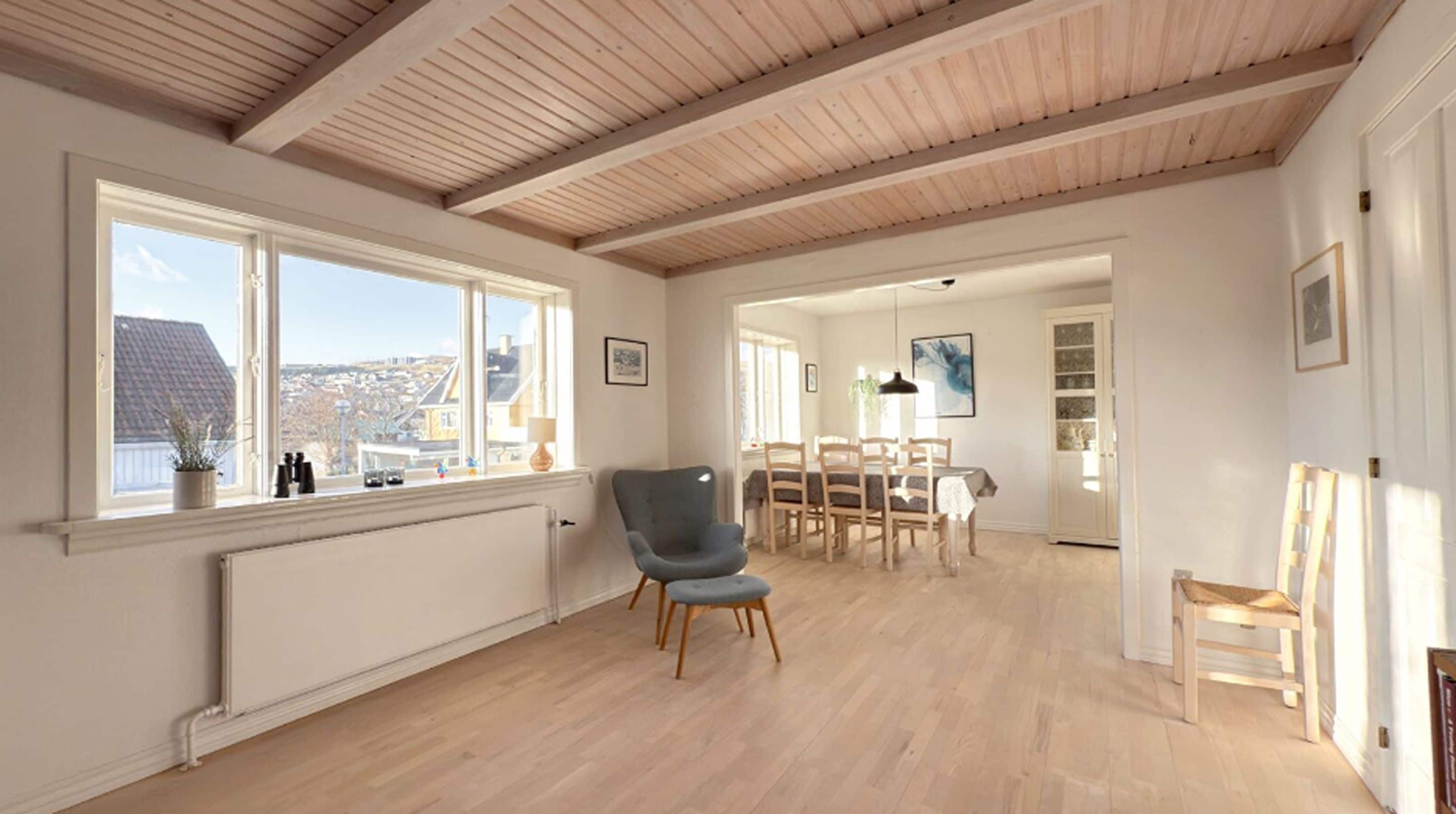 Una habitación amplia con techo alto, zona de comedor con mobiliario de madera y vistas a través de grandes ventanales.