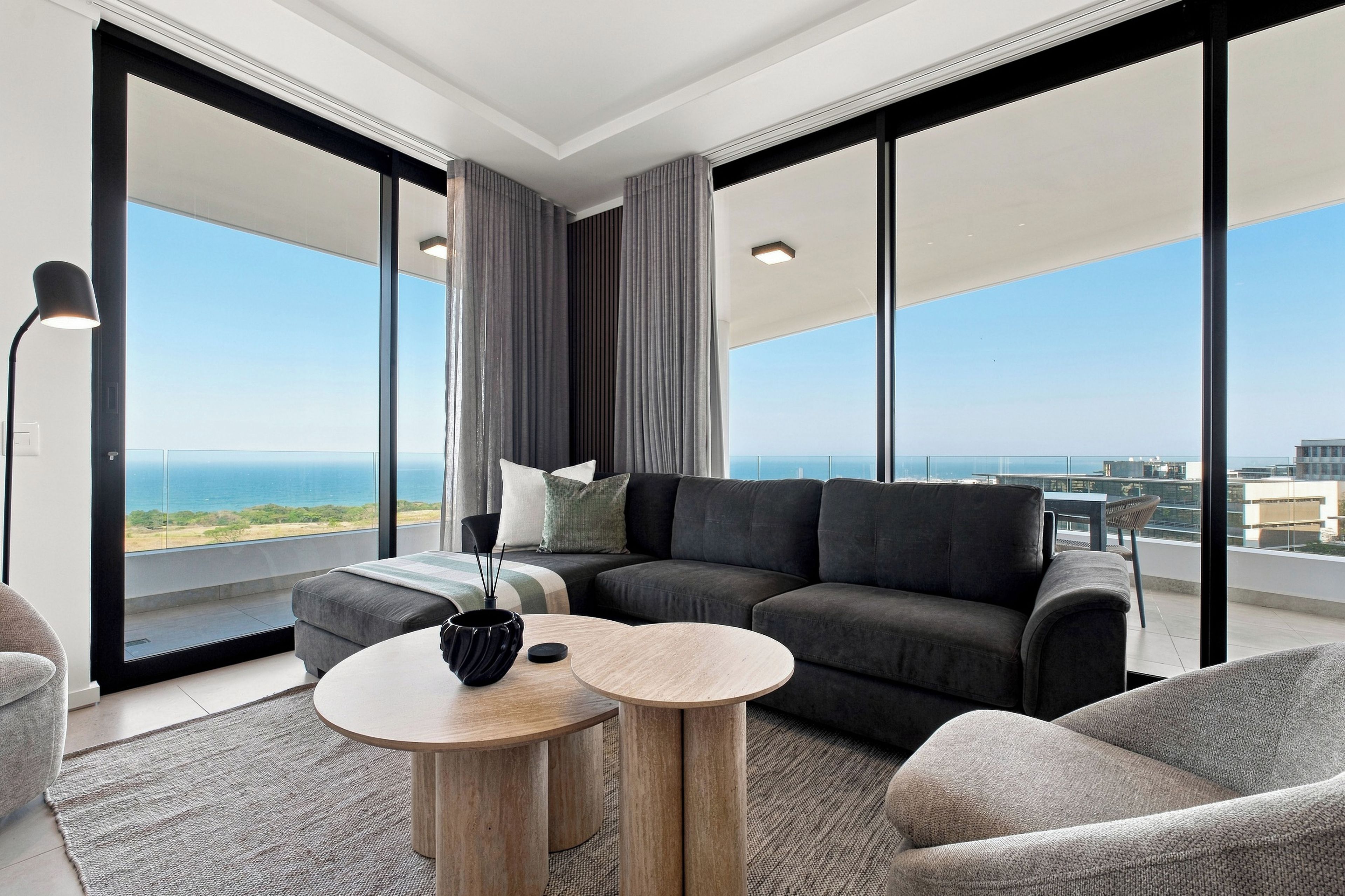Ein modernes Wohnzimmer mit einer Couch, zwei runden Tischen und Meerblick.