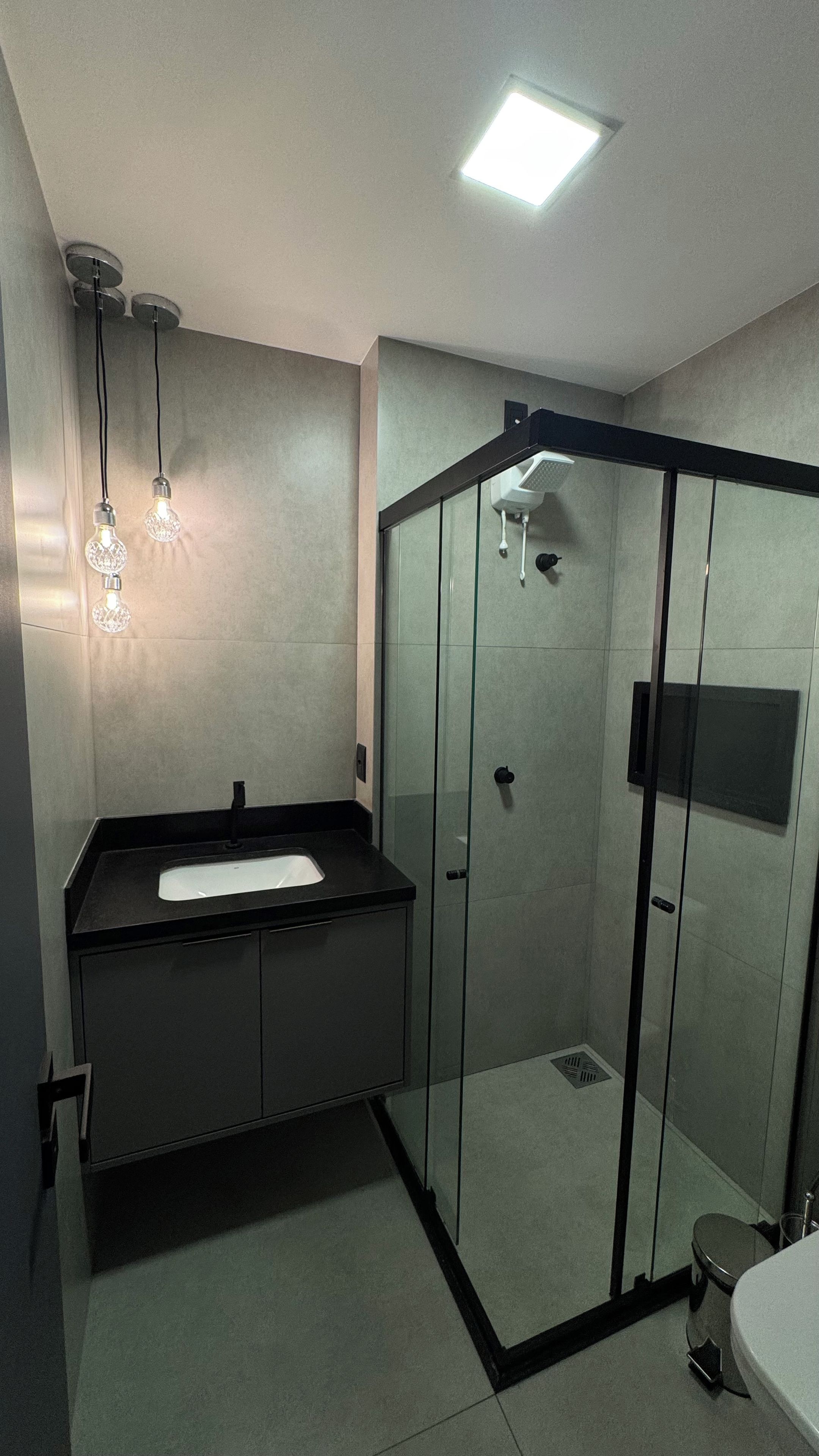 Un baño moderno con cabina de ducha de vidrio, encimera negra y lavamanos blanco.