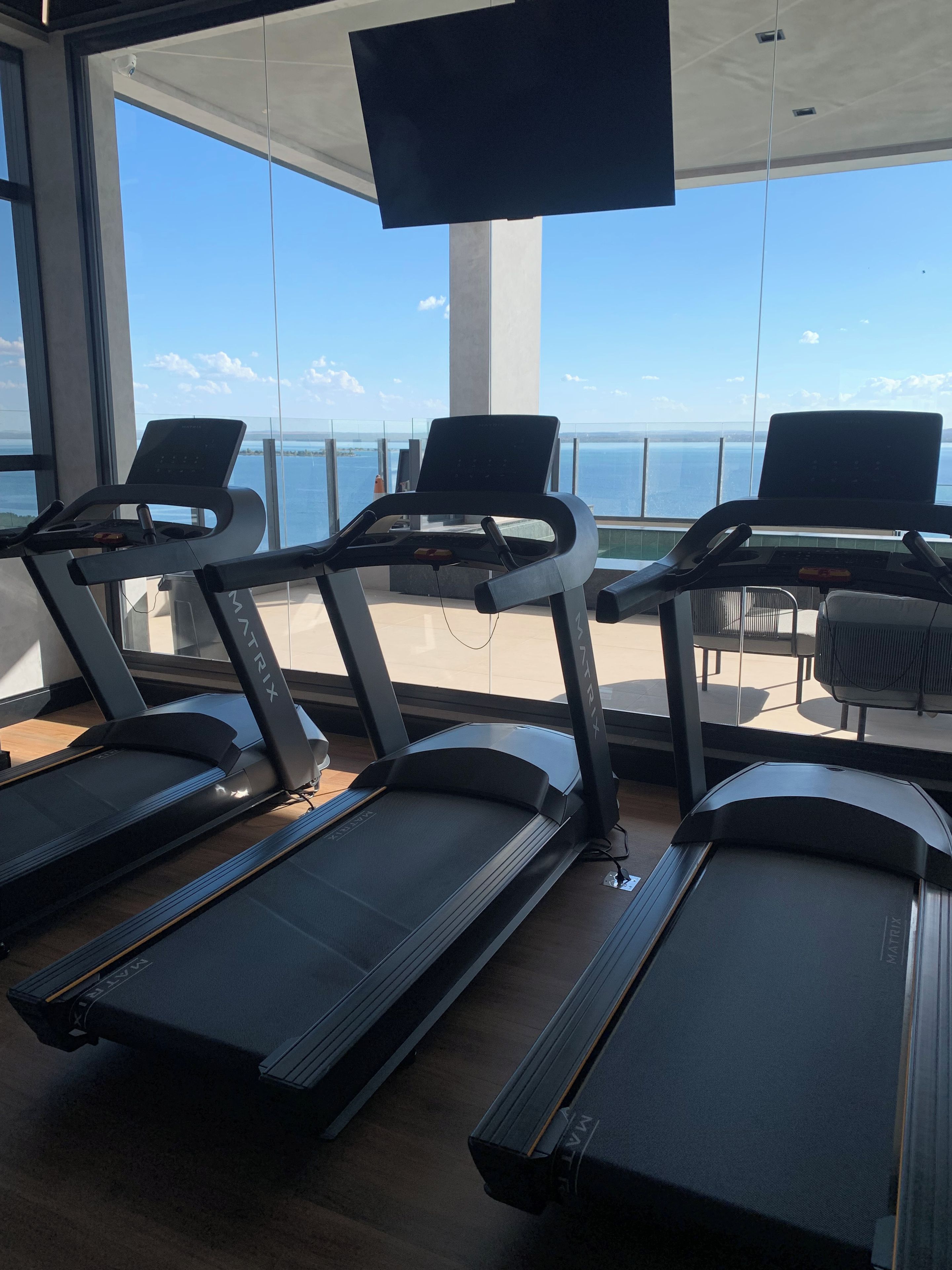 Un gimnasio con cintas de correr y equipamiento de ejercicio, con vista a un cuerpo de agua.