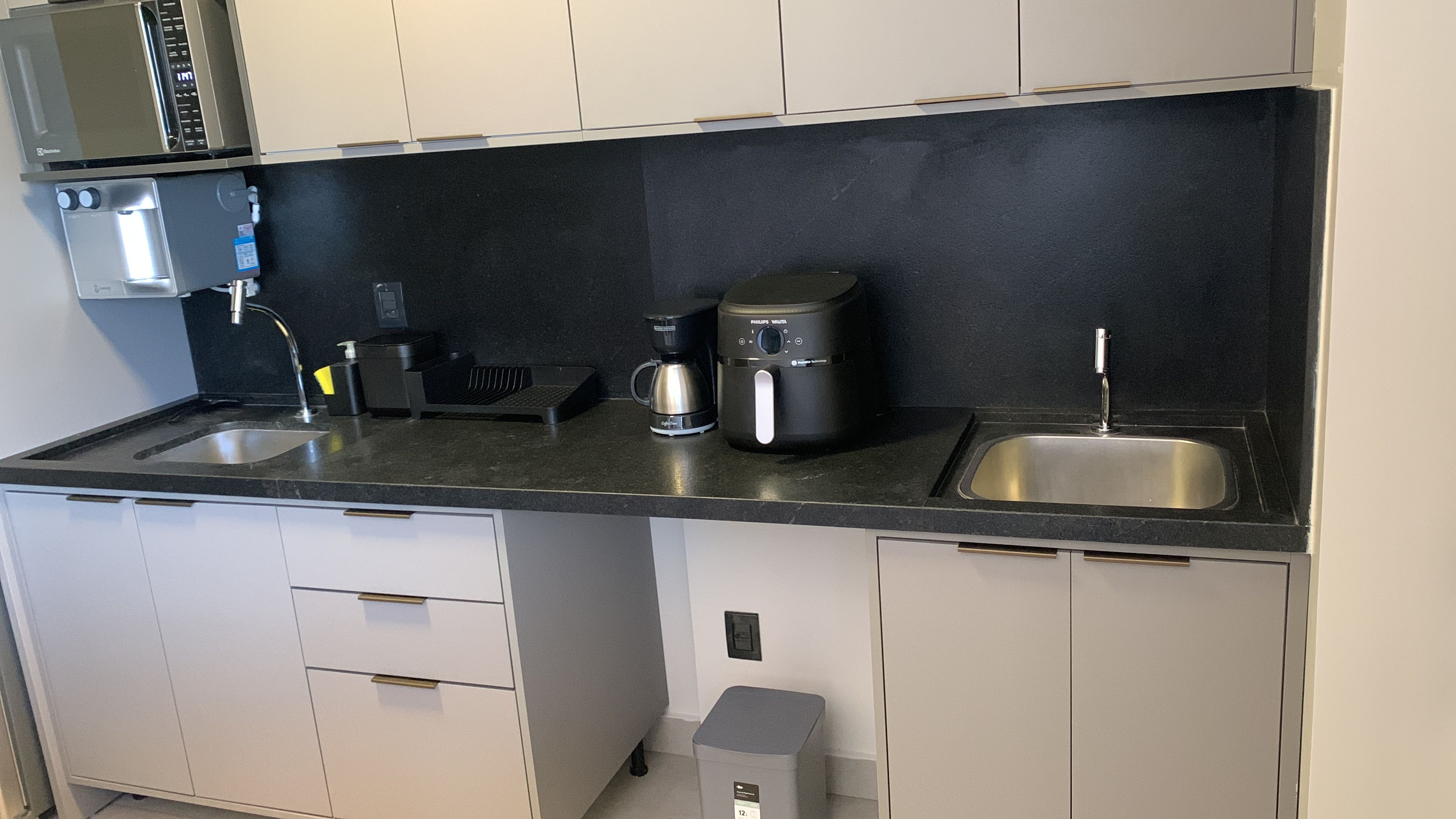 Una cocina moderna con microondas integrado, cafetera y lavabo.