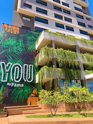 Un bâtiment moderne orné d’une fresque représentant des feuilles de palmier et du mot « VOUS », œuvre de Fama.
