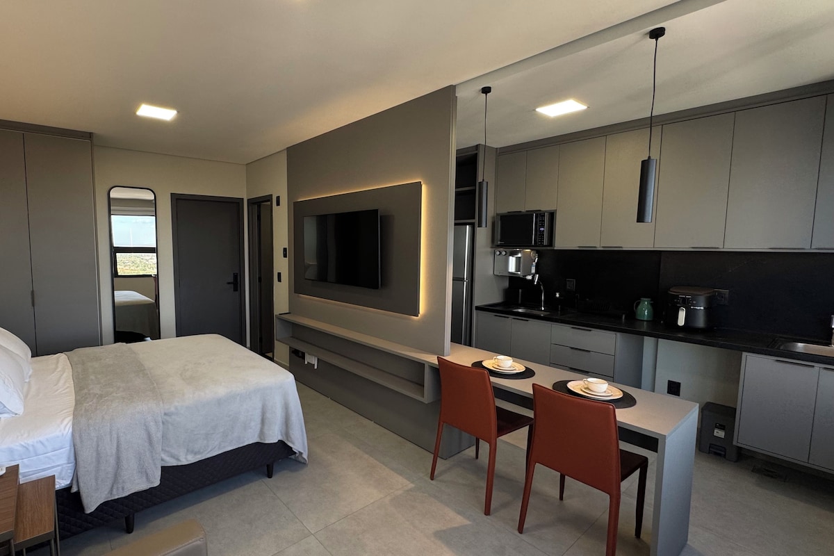 Une chambre d’hôtel moderne équipée d’un lit, d’une table de chevet, d’une télévision, d’une kitchenette et d’un petit coin repas.