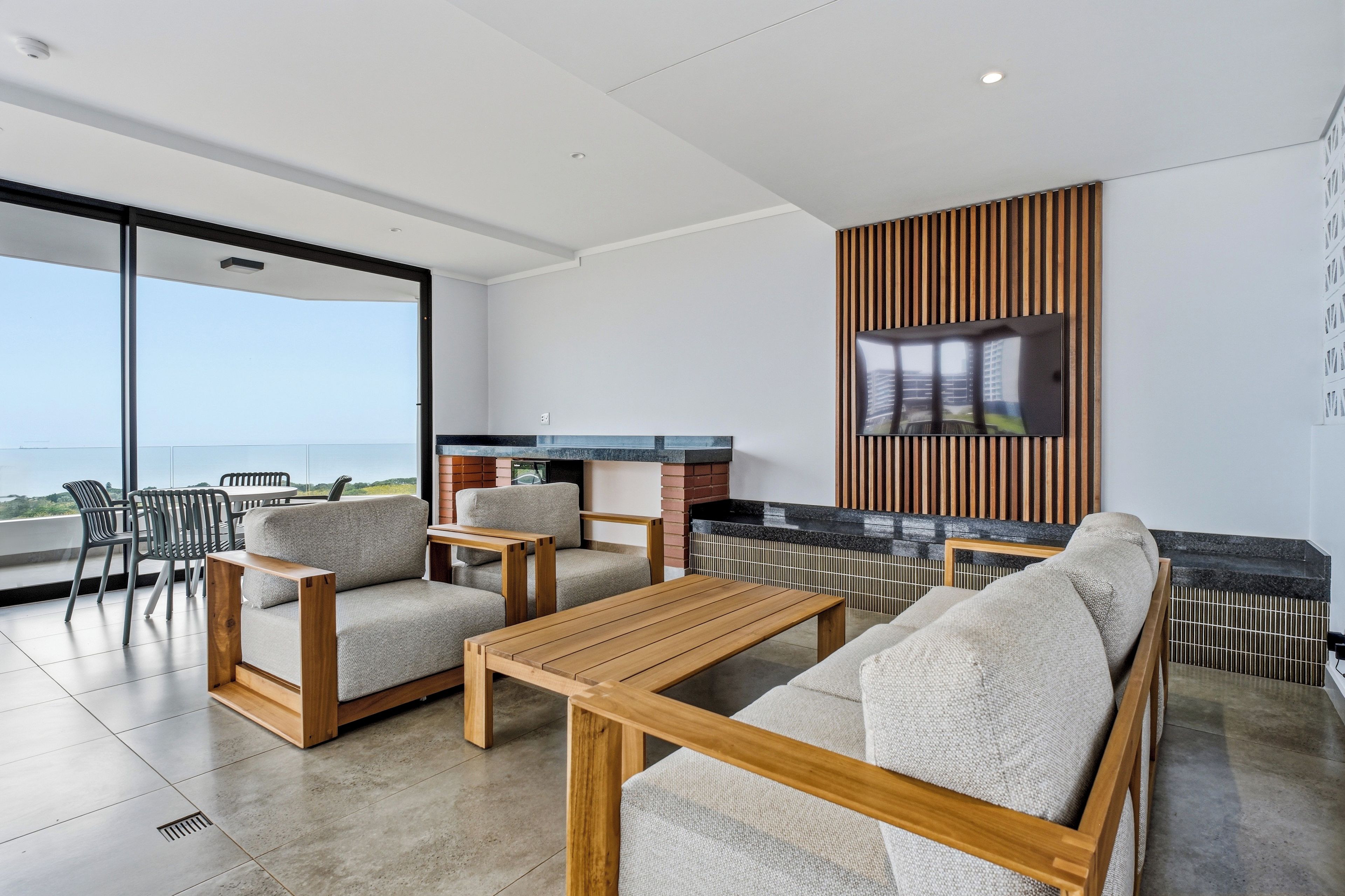 Una sala de estar moderna con sofá, sillones, una mesa de centro y un televisor montado en una pared de paneles de madera.