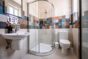 Een badkamer met een douchecabine van glas, een witte wastafel en een toilet.