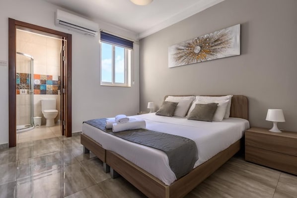 Een slaapkamer met een groot bed, nachtkastjes, een douchegedeelte en een raam.