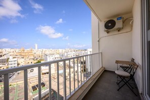 Ein Balkon mit Blick auf eine Stadtlandschaft, eine Klimaanlage und ein kleiner Tisch mit einem Stuhl.